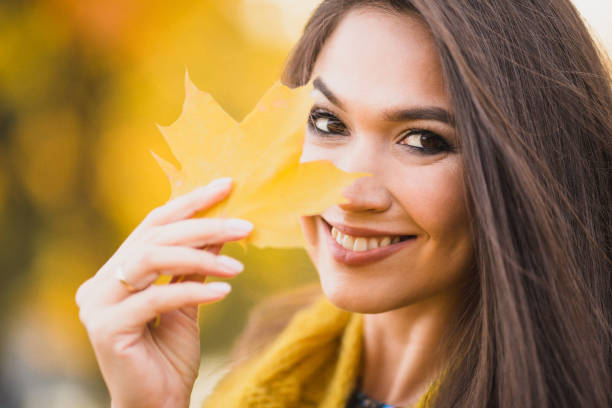 istock Charming brunette girl hides a smile behind a yellow maple leaf 1603807517