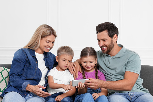 Happy family with smartphone spending time together on sofa at home