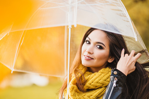 Attractive seductive brunette woman with a gaze under a transparent umbrella in the fall