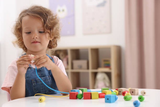 motor skills development. little girl playing with wooden pieces and string for threading activity at table indoors - 4 string imagens e fotografias de stock