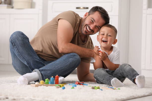 istock Motor skills development. Father and son playing with wooden pieces and string for threading activity on floor indoors 1603810189