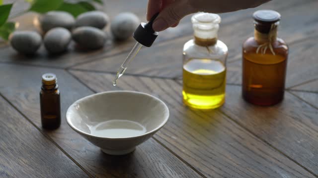 Essential oil droppind from dropper to bowl with base oil on wooden background.
