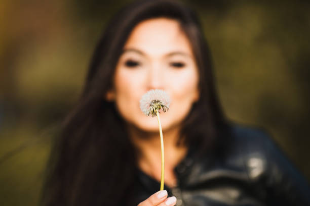 istock Young cute graceful brunette Asian blowing on a dandelion 1603814447