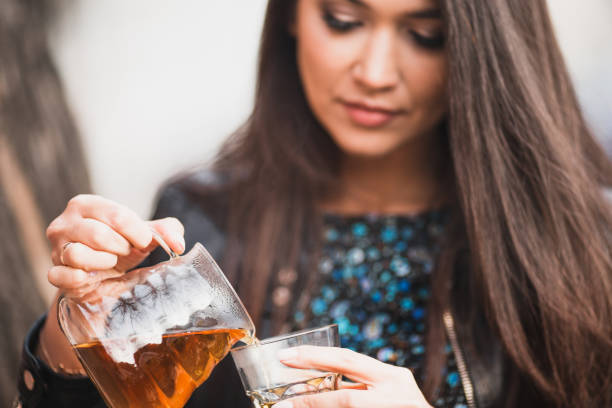 Attractive brunette with luxurious hair pours tea from a glass teapot into a glass