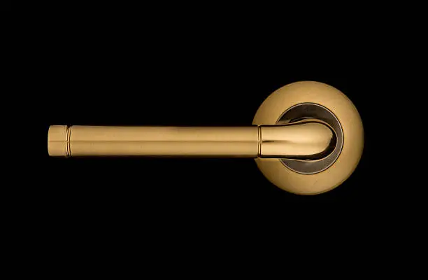 Door handle of the yellow metal isolated on a black background