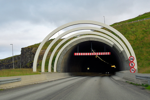 Asphalt road is twisting along sheer cliffs overgrown with lush greenery. Highway is winding through picturesque European Alps in summer.