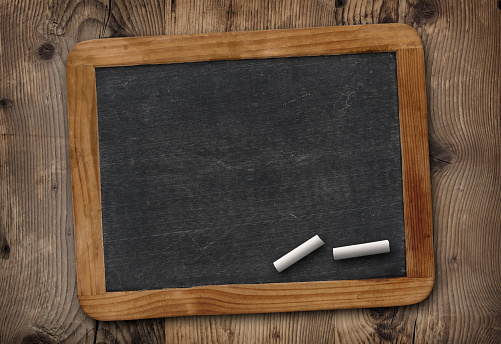 Colorful chalks and duster on wooden table near black board. Space for text