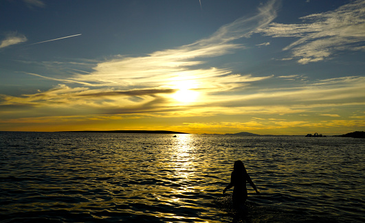 Silhouette of a woman bather entering the sea during the golden hour and sunset