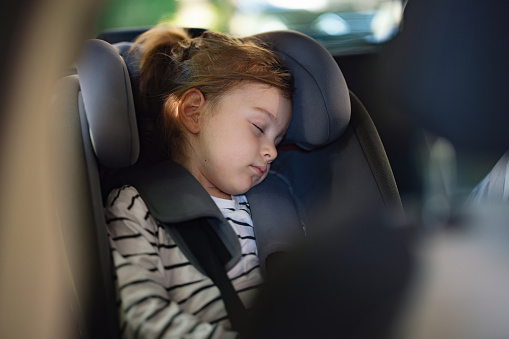 Close up shot of an adorable little girl sleeping in a child car seat. She is resting while going on a car ride.