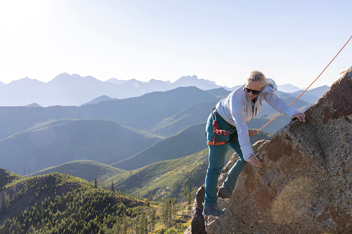Man belays from summit boulder, woman climbs below