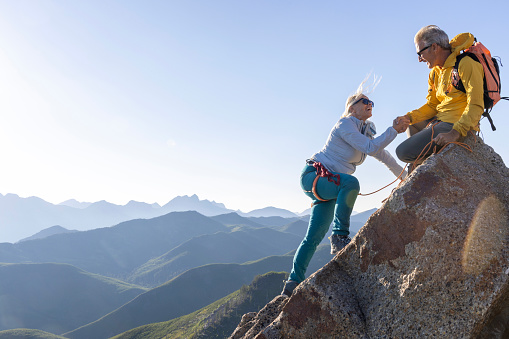 Man belays from summit boulder, woman climbs below