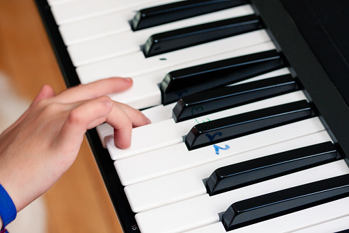 Mexican teen girl with disability practicing piano at home, close up of fingers playing piano keys with marks