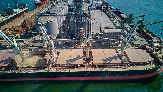 Loading grain into holds of sea cargo vessel in seaport from silos of grain storage. Bunkering of dry cargo ship with grain. Aerial top view.