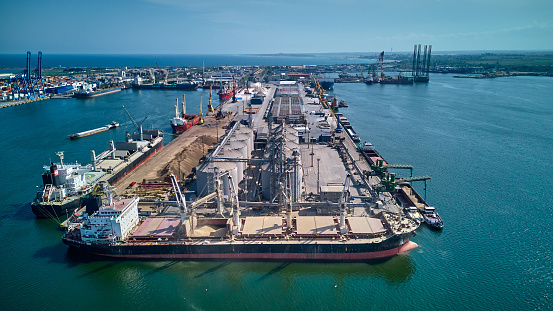 Loading grain into holds of sea cargo vessel in seaport from silos of grain storage. Bunkering of dry cargo ship with grain. Aerial top view.