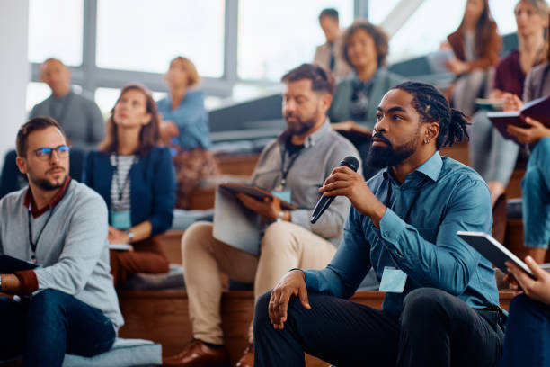 istock Black entrepreneur asking a question while attending business seminar in conference hall. 1604032414