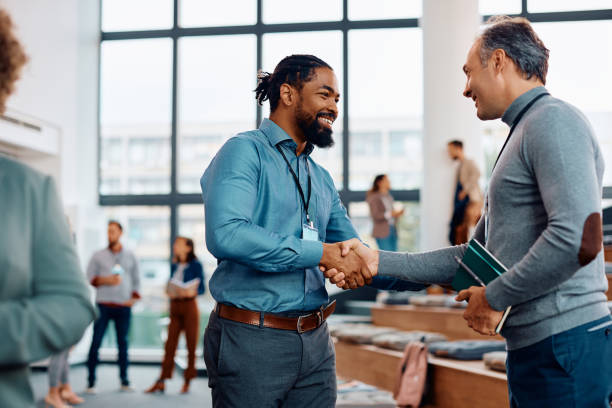 Happy businessmen greeting while attending an education event at conference hall. Happy black entrepreneur handshaking with a colleague while attending business conference at convention center. press room stock pictures, royalty-free photos & images