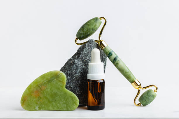 istock Green jade roller massager for face on white marble. 1604069950