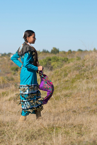 A young female performing a jingle dress dance in a prairie field