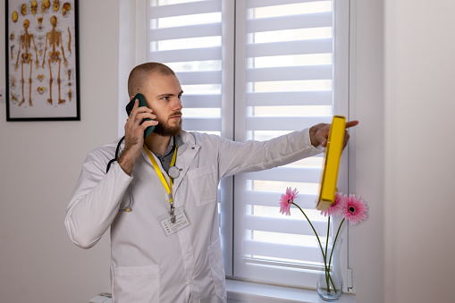 A young Caucasian male doctor resting a bit in office talking on the phone