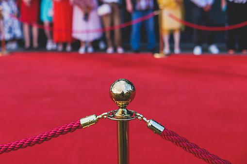 Red carpet with ropes and golden barriers on a luxury party entrance, cinema premiere film festival event award gala ceremony, wealthy rich guests arriving, outdoor decoration elements, a summer day