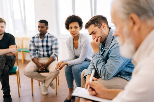 istock Selective focus portrait of pensive man telling about mental problem or addiction to other patients sitting in circle during group therapy session. 1604175774