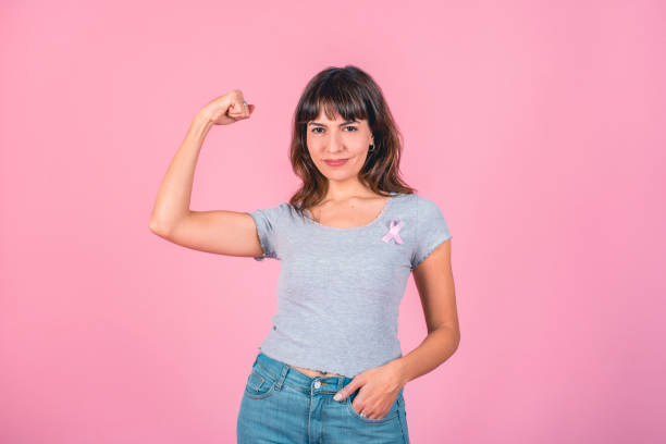 A woman wearing pink breast cancer awareness ribbon while showing arm muscle. Victory over breast cancer. A woman wearing pink breast cancer awareness ribbon while showing arm muscle. Victory over breast cancer. brest cancer hope stock pictures, royalty-free photos & images