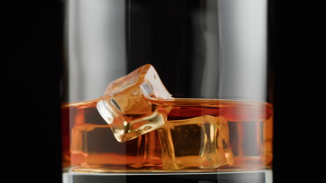 Brandy or whiskey with ice close-up. Luxury cognac on black background. Alcohol amber drink, drinking rum, liqour beverage in glass.