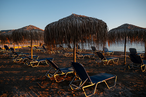 Rocky beach with sun beds and umbrellas at sunrise.