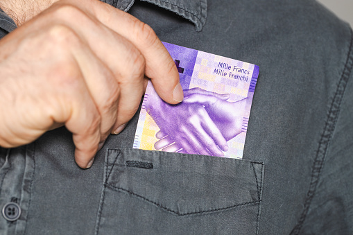 The man takes a thousand Swiss francs out of his shirt's pocket, the highest denomination of paper money in Switzerland, business concept, 1000 francs banknote