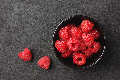 Raspberry in black bowl on dark background. Fresh red berries. Healthy food. Natural vitamins. Top view.