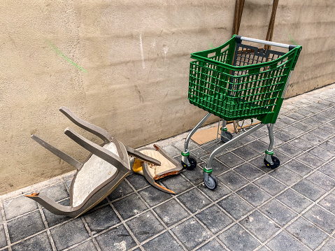 High angle view of broken chair and shopping cart side by side left in the street in the city of Valencia, Spain
