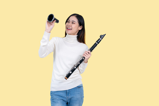A beautiful and talented young Asian woman holding a clarinet while standing against an isolated yellow background. musician, artist, jazz instruments