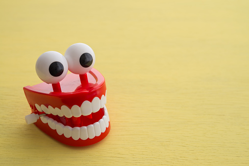 Chattering teeth toy or joke teeth wind up moving on yellow background. Funny, comedy, relax time concept.