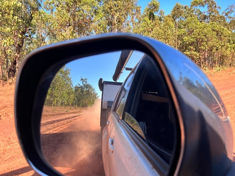 Mirror reflection of car towing an off road caravan driving on Peninsula Development Road DPR of Cape York Peninsula in Queensland, Australia