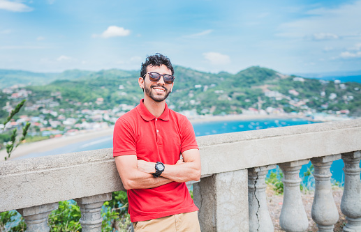 Portrait of smiling tourist in a viewpoint of a bay. Handsome tourist man looking at the bay of San Juan del Sur