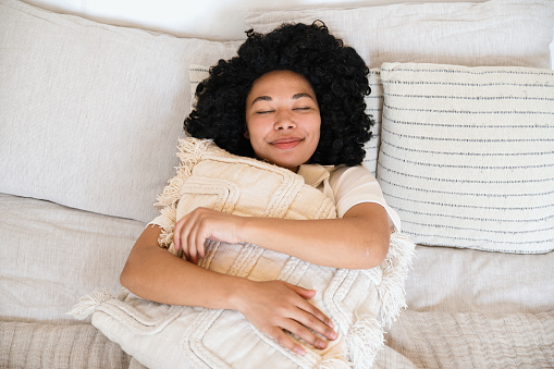 top view of smiling african american woman sleeping in soft bed and hugging pillow. dreamy female with closed eyes resting and imagination in cozy bedroom.