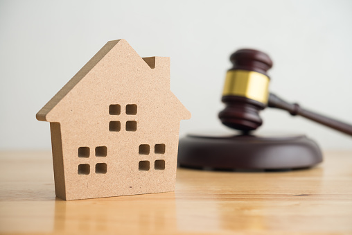 Simple house model, hammer judge gavel on wooden table with white wall background. Foreclosure, bankruptcy concept. Person is unable to reply outstanding debts or obligations, stops mortgage payment.