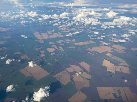 View of the land, fields, and clouds from above. Aerial view landscape covered with puffy cumulus. Airplane point of view of cloudy landscape.