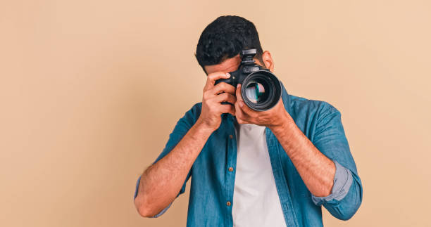 istock Young photographer standing and holding camera on brown background. 1604636900