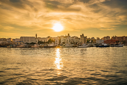 Sunset reflection shimmers and dances on the gentle ripples of the water over the Port of Monopoli, creating a pathway of glistening light that leads straight to the heart of the harbor