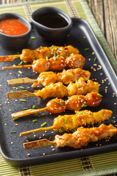Japanese yakitori skewers served with two sauces close-up on a plate. Vertical Japanese yakitori skewers served with two sauces close-up on a plate on the table. Vertical sticky sesame chicken sauces stock pictures, royalty-free photos & images