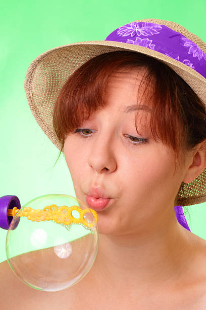 Beautiful young girl in hat blowing soap bubbles stock photo