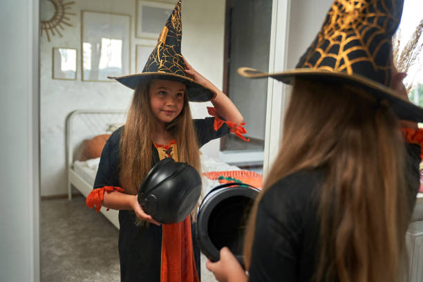 istock Elementary age girl wearing witch costume and looking in the mirror 1604720602