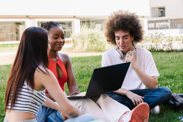 multiethnische gruppe von freunden, die zusammen auf dem gras sitzen - computer student mixed race person multi ethnic group stock-fotos und bilder