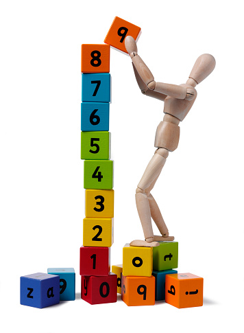 Wooden mannequin holding coloured building blocks with numbers. Isolated on white