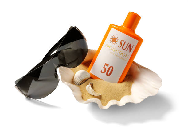 Sun protection in a sea shell with sand and sunglasses, isolated on white with clipping path.