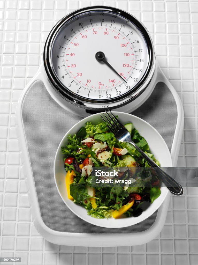 Bathroom Scales and Healthy Eating Bathroom scales on a tiled floor with a bowl of salad. Balance Stock Photo