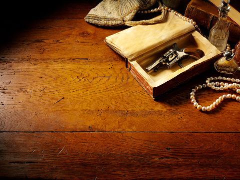 Vintage themed image of a Edwardian gun, snuff bottle and pearls on a old wooden table. Copy space