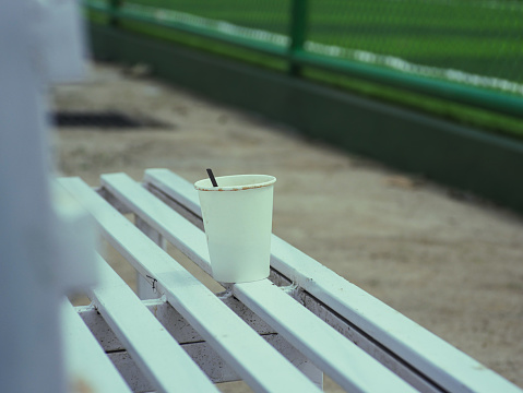coffee cup left on a long wooden park bench. lonely concept
