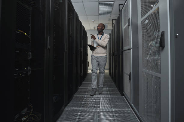 istock Technician, cybersecurity and man in the server room for data maintenance, it or analysis. System, engineer and African male coder or programmer doing inspection on information technology in office. 1604805245